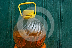 A large plastic bottle with sunflower oil closed with a yellow cork against the green wall