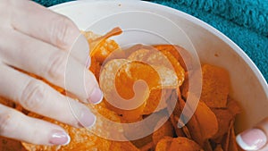 Large plate with potato chips. The woman lies on the couch and eating potato chips, close up view