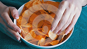 Large plate with potato chips. The woman lies on the couch and eating potato chips, close up view