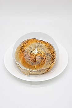 Large Poppy Seed Bagel filled with Cream Cheese on a White Plate with a White Background