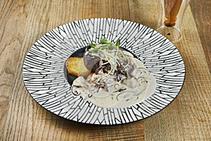 Large portion of delicious beef steak with creamy mushroom sauce and fried potatoes in a ceramic plate on a wooden background