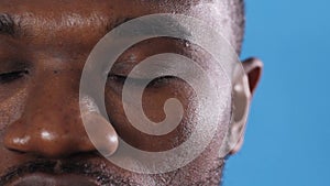 large portrait of an African American man opening his eyes on a blue background.