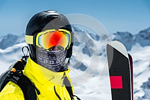 A large portrait of a skier in a protective helmet and glasses - a mask and a scarf next to the skis against the snow