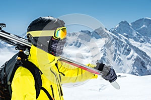 A large portrait of a skier in a protective helmet and glasses is a mask and scarf with skis on his shoulder in the snow