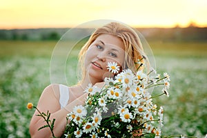 A large portrait of a young, plump, beautiful woman resting on a chamomile field at sunset. A plus-size woman in a white sundress