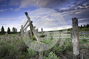 Large post at the end of a barbed wire fence in a green hilly setting under the cloudy sky