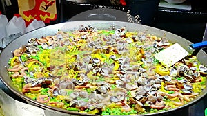 Large pot of spanish seafood named paella cooking at public food market, typical food of a part of spain, healthy and nutrition