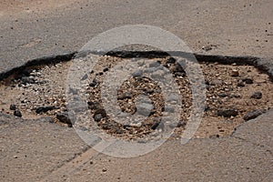 Large pothole in city street creates hazardous driving conditions for passing vehicles.