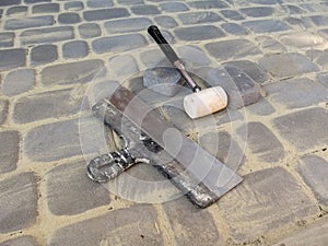 A large putty knife, a white rubber mallet and two bricks lie on the surface of the new paving slabs. The concept of laying paving