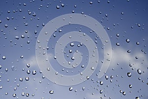 Large rain drops on the window glass with dark blue sky and clouds. Selective focus