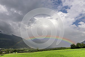 A large rainbow emerges from the clouds over an apple planted field in Val Venosta, Prato allo Stelvio, Italy