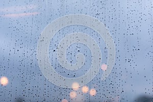 Large raindrops on the glass surface of the window, heavy rain showers weather, evening city lights defocus. Backdrop wallpaper