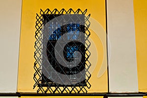 A large rectangular window of a yellow stone building closed by a large black iron grate. The background