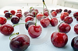 Large red cherries with twigs and a light background are covered with water drops.