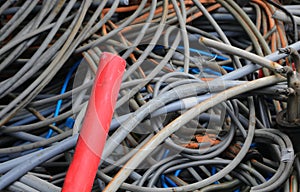 Large red electrical cord and many other tangled used electrical cords in landfill for recycling copper and polluting plastic