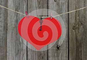 Large red heart sign with key hanging on clothesline by old weathered wood fence