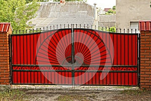 Large red metal gates on a brick fence in the street