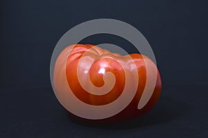 A large red tomato on a black background. Vegetables close-up