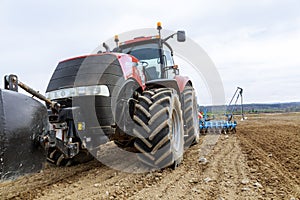 A large red tractor close-up with sowing equipment stands in a field.