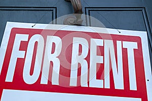 A large For Rent sign white text on red background is attached to  metal door handle on the front door