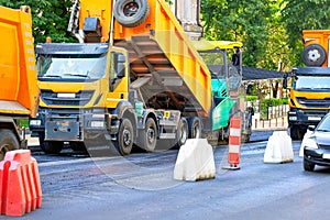 Large road construction equipment is actively working on the city street, laying a new asphalt pavement on the road