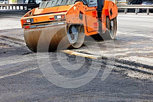A large road vibratory roller rolls off the highway to lay fresh asphalt on the new road