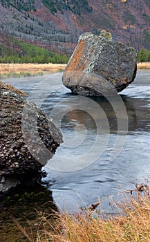 Large rock boulder rests in the flowing river perpendicular view