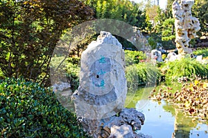 A large rock formation on a deep green lake surrounded by lush green trees in a Japanese garden