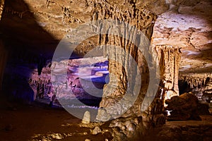 Large rock formations in cave with waxy surface and glow of purple in the background