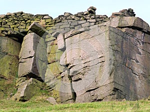 Large rock outcrop boulders with a stone wall along the top in yorkshire moorland