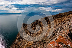 Large rock with red stones on Lake Baikal. The sky in the clouds. On the water ripples.