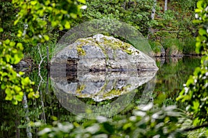 Large rock reflected in calm water surface