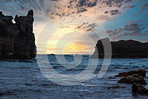 large rocks in the ocean with a cloudy sky above them