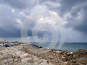 Large rocks on the shores of the Mediterranean Sea, dramatic skies and rain over the largest sailing yacht in the world, an eight-