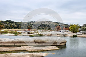 Large rocks in the water in the Pedernales River in the autumn in Texas with tourists sitting on rocks in distance and insulators