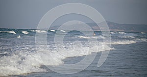 A large roll of sea waves, an unknown sportsman-surfer walks with a surfboard and rolls on the waves. The athlete goes