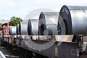 Large rolls of sheet metal lying on a freight wagon pulled by locomotives.