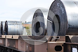 Large rolls of sheet metal lying on a freight wagon pulled by locomotives.