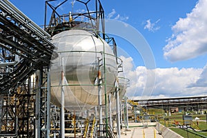 A large round ball-shaped shiny metallic high-pressure iron storage tank for ammonia is strong with pipes and equipment