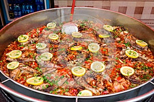 Large round pot with fish sour soup known as borscht with red tomatoes, decorated with fresh yellow lemon slices, ready to eat hea