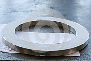 A large round shiny metal ring with small holes, holes, a flange on the working iron table in the factory, the workshop.