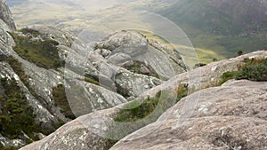 Large round stones covered with moss, grass and bushes growing around, green valley background, typical scenery seen during trek