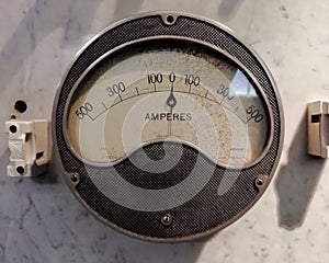 a large round vintage industrial ammeter with an analogue dial with numbers with standard electrical symbols on a white dial on a