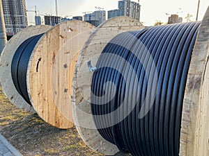 Large round wooden spools of bobbins with wires, black electric cables in rubber insulation, used in the wiring of conductor lines