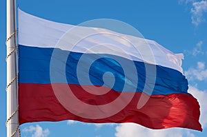 Large Russian flag against the blue sky with clouds close-up. State symbol of the Russian Federation in the wind. The