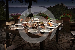 Large rustic table on a garden terrace prepared for a dinner party at night