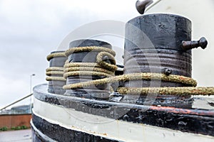 Large rusty bollards with coiled ropes on a ship against a gloomy sky. Mooring in the port. Close-up