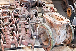 Large rusty old metal gate valve, pipe fittings, against the background of small valves, pipeline valves in the factory, shop. Con