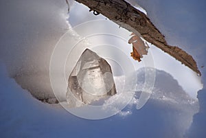 Large shining crystal of transparent quartz in the sunlight on the snow winter background close-up