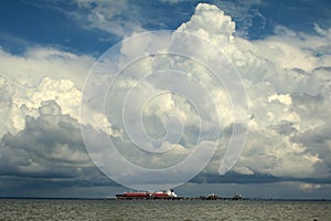 Large ship/boat in ocean water with clear blue skies and large white clouds.